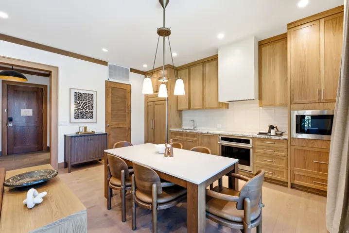 Open-concept kitchen and dining area featuring wood-finish flooring, light wood cabinetry, white subway tile backsplash, and stainless steel appliances