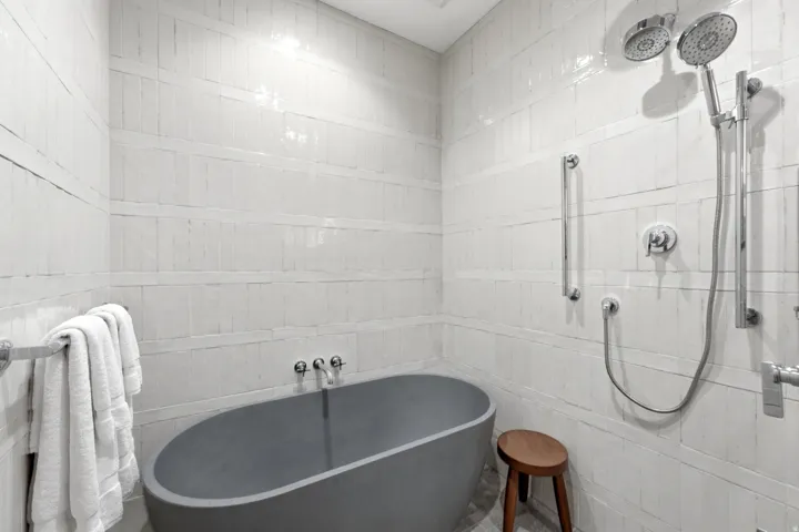 Freestanding soaking tub, floor-to-ceiling tile surround, dual shower heads, and chrome fixtures