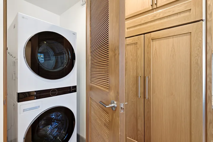 Stacked washer and dryer unit, wood-finish cabinetry, louvered wood-finish door, satin nickel door hardware, stainless steel cabinet pulls