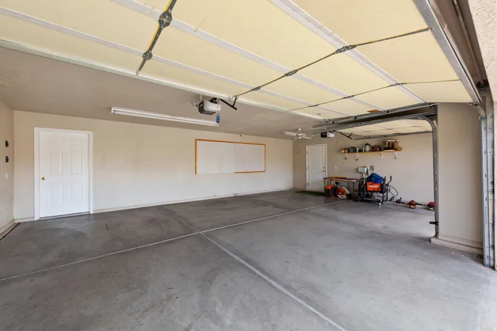 Spacious garage with concrete flooring, two paneled interior doors, fluorescent lighting, and an automatic garage door opener