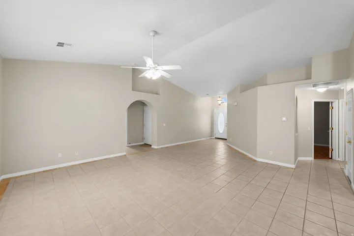 Vaulted ceiling, ceiling fan, tiled flooring, arched doorway, and a front entry door with an oval glass insert