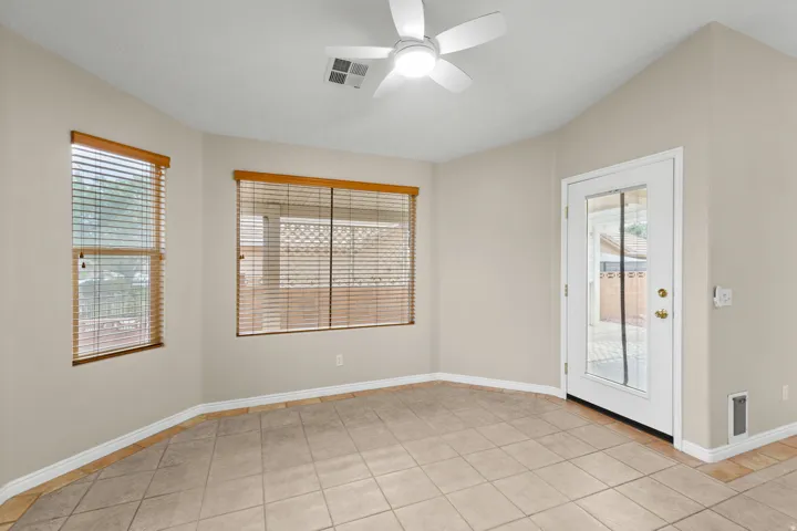 Tiled flooring with neutral wall tones, two windows with wood blinds, a ceiling fan, and a glass-paneled door