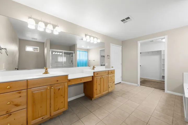 Dual vanities with integrated sinks, ample counter space, custom wood cabinetry, extensive wall mirror, and tile flooring