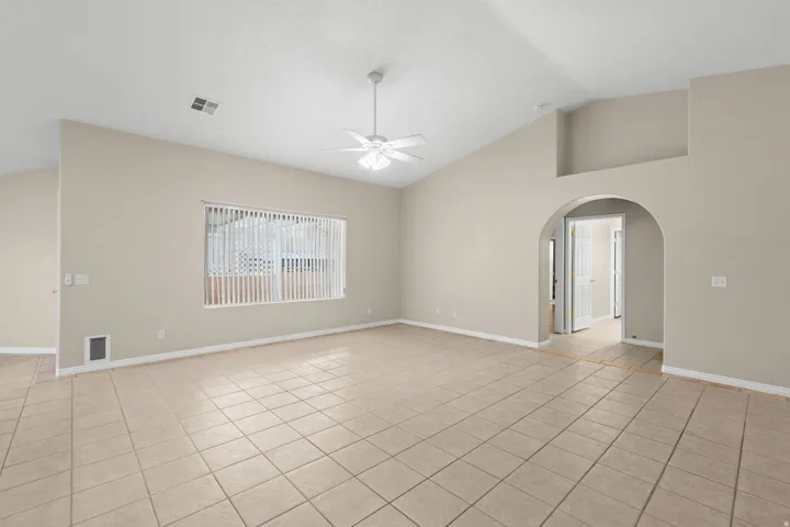 Vaulted ceiling, ceiling fan, tiled flooring, window with vertical blinds, and an arched doorway