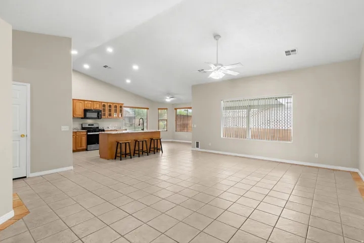 Vaulted ceilings with recessed lighting, tile flooring, and a kitchen featuring wood cabinetry, a center island with a breakfast bar, and a pull-down faucet