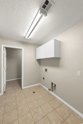 Utility area featuring tile flooring, white wall cabinets, a fluorescent light fixture, and laundry hookups
