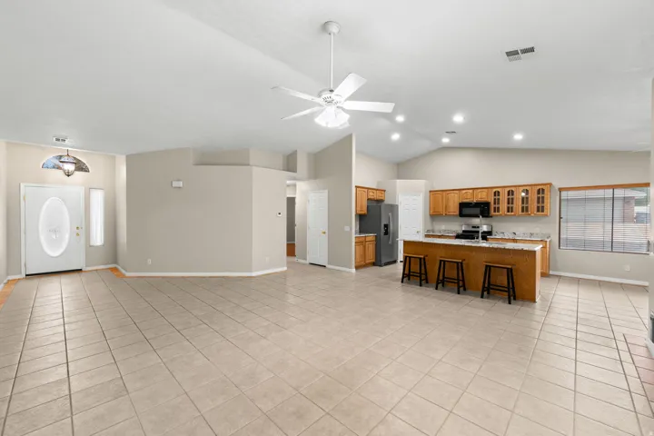 Vaulted ceilings, a ceiling fan, and recessed lighting illuminate this open-concept space featuring tile flooring