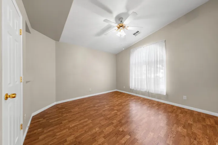 Vaulted ceiling with a ceiling fan, window with sheers, wood-finish flooring, and a white paneled door with brass hardware