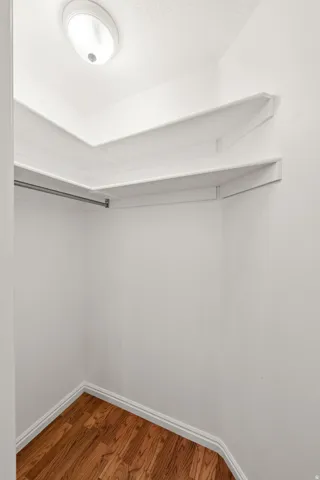 Recessed ceiling light fixture, white shelving, clothing rod, and wood-finish flooring