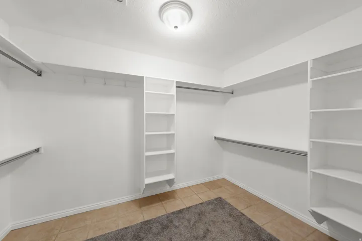 Recessed ceiling light fixture, built-in shelving, multiple clothing rods, and tile flooring