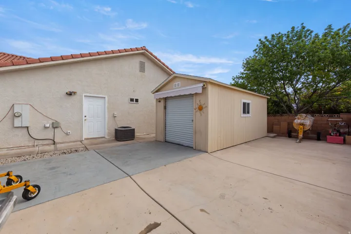 Stucco exterior with a terracotta tile roof, concrete patio, and a separate workshop with a roll-up door and awning