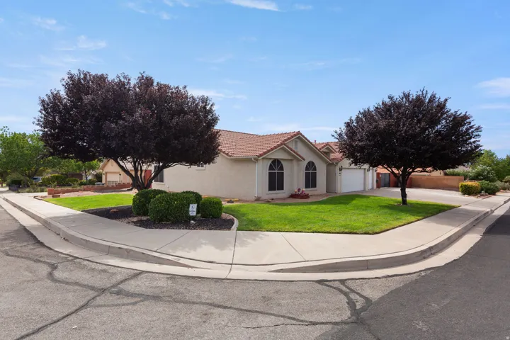 Stucco exterior with a tile roof, arched windows, attached garage, and mature trees
