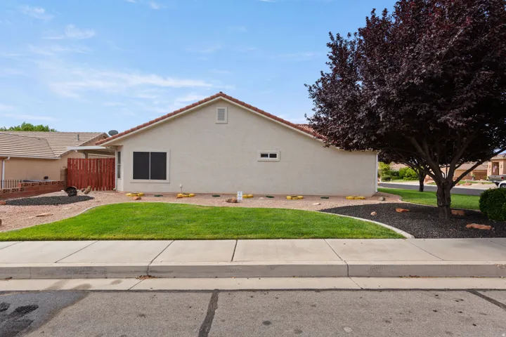 Stucco exterior with a terracotta tile roof, partial privacy fence, and mature tree
