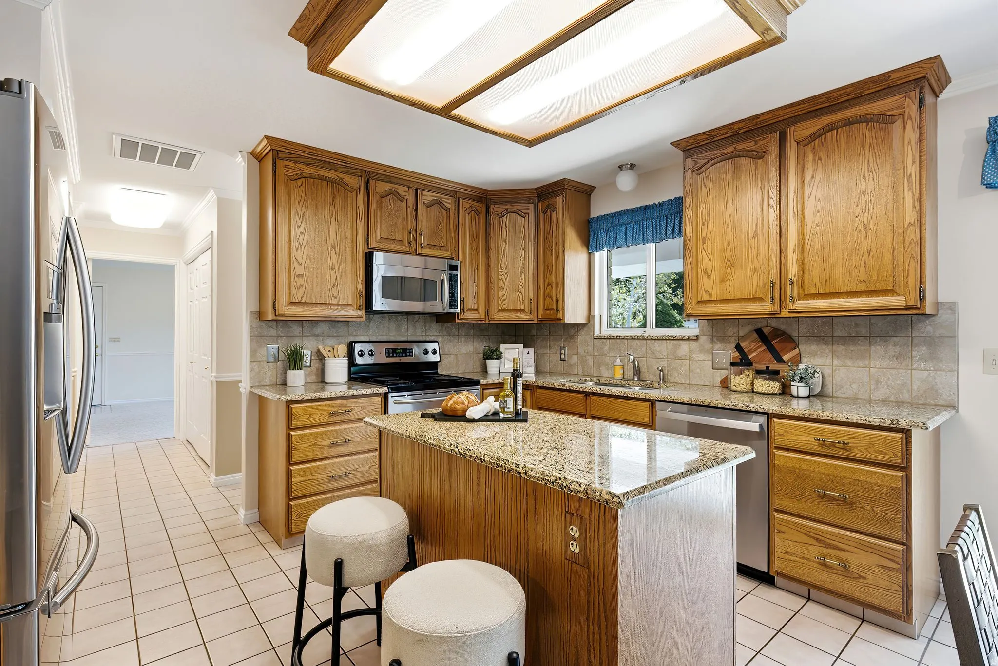 Kitchen featuring wood cabinetry, stainless steel appliances, a center island with granite countertop, and tiled flooring