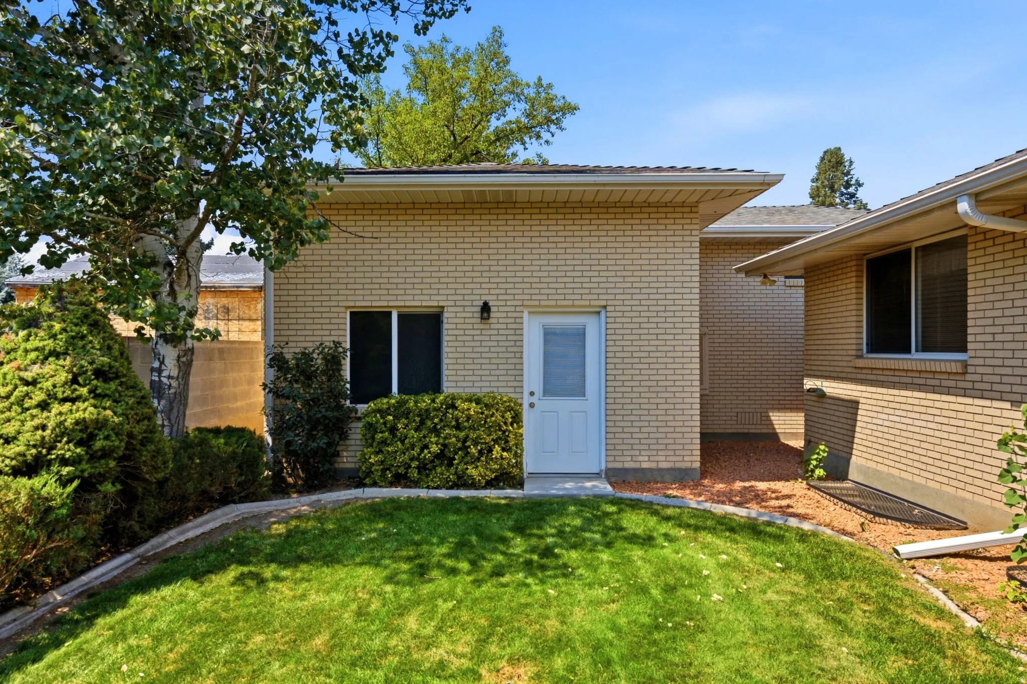 Yellow brick exterior with a white entry door, framed by landscaping and a manicured lawn