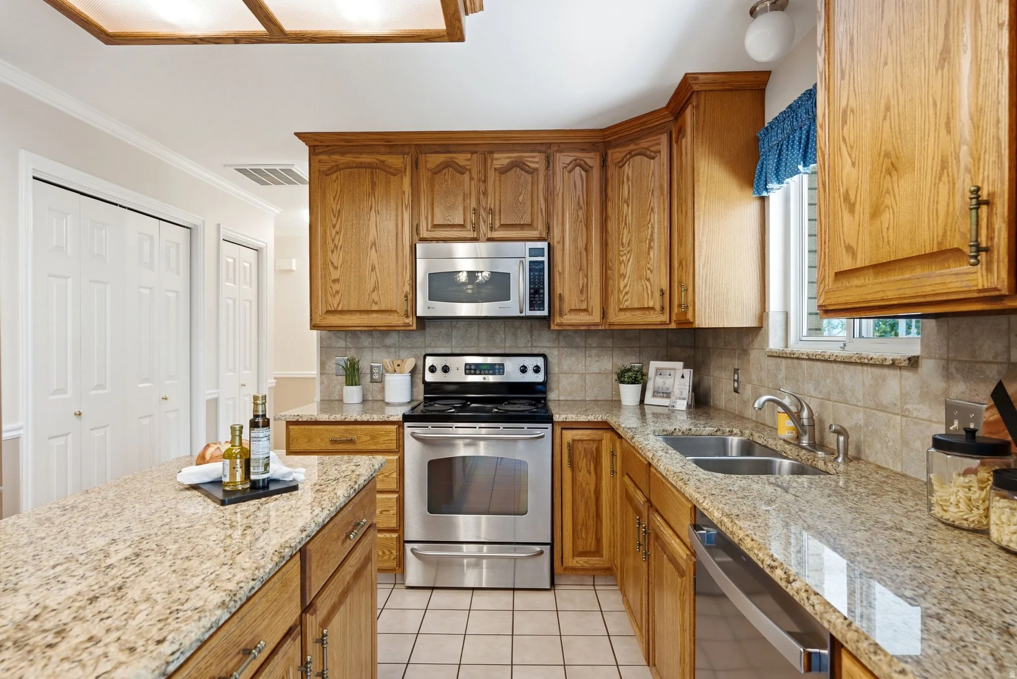 Kitchen featuring wood cabinetry, stainless steel appliances, granite countertops, tile flooring, and a tile backsplash