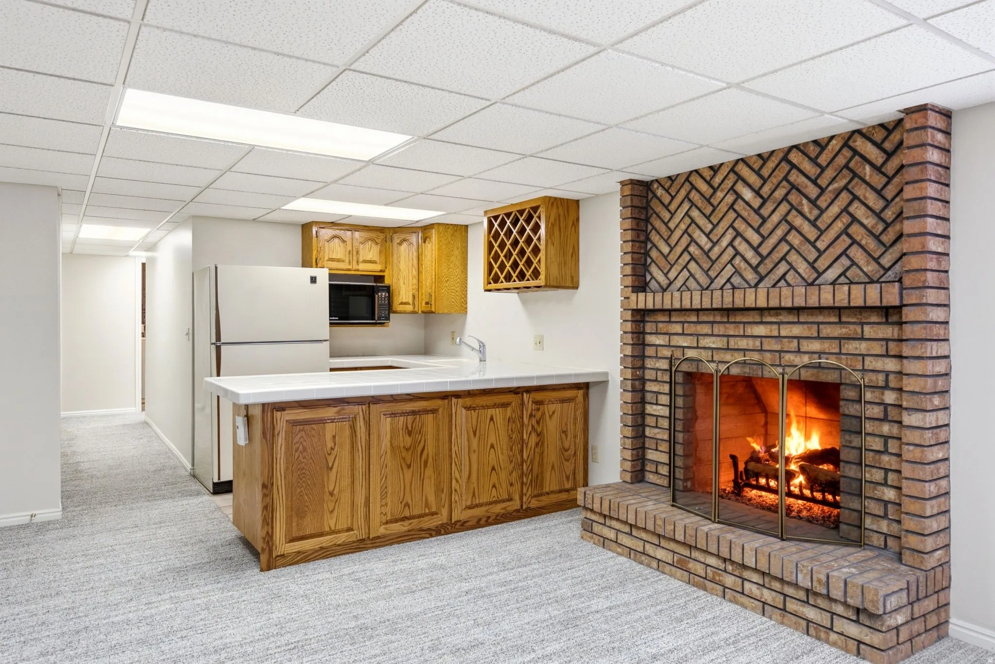 Brick fireplace with hearth, built-in wet bar, wood cabinetry, built-in microwave, and drop ceiling with integrated lighting
