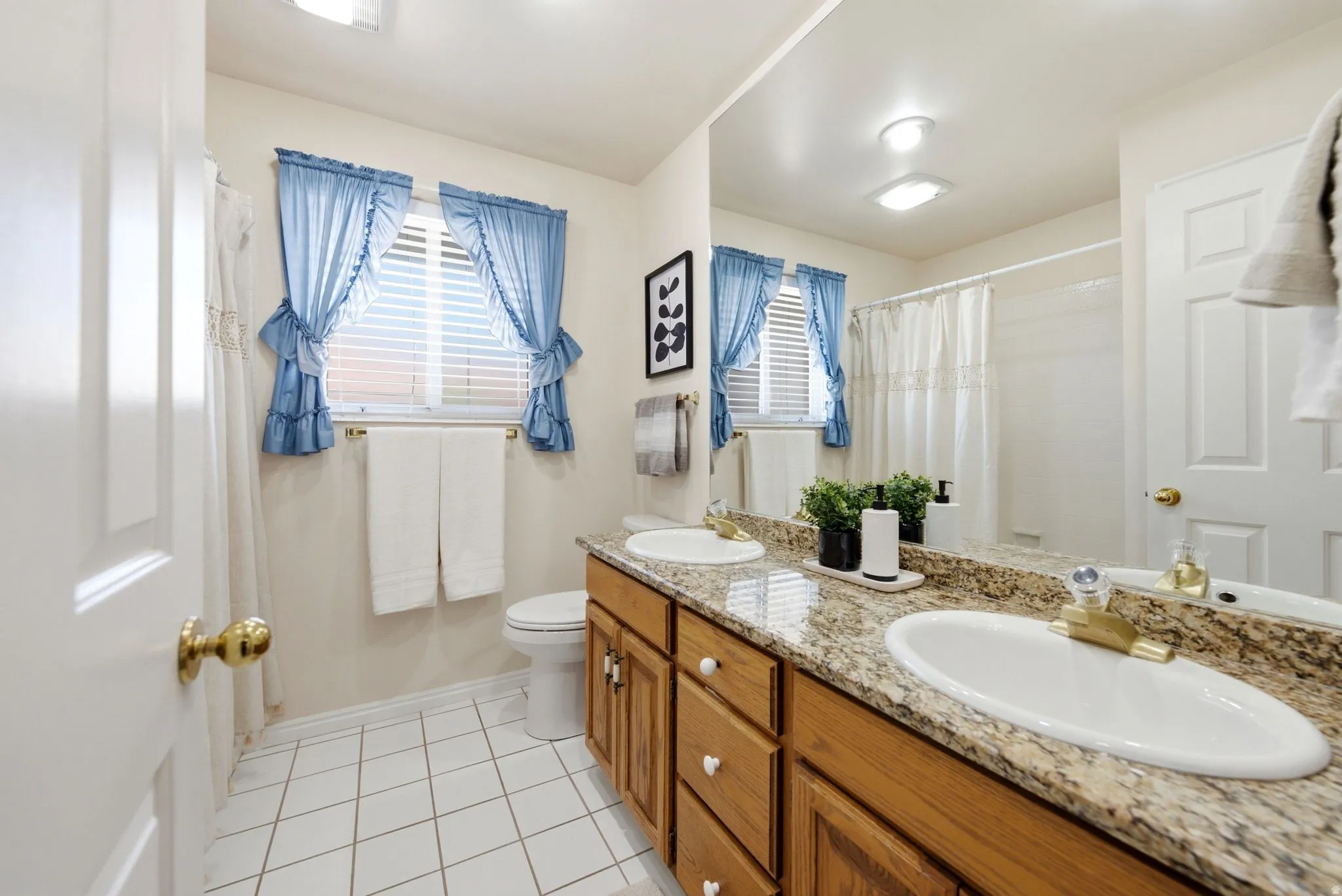 Double vanity with undermount sinks, stone countertop, wood-finish cabinetry, and ceramic tile flooring