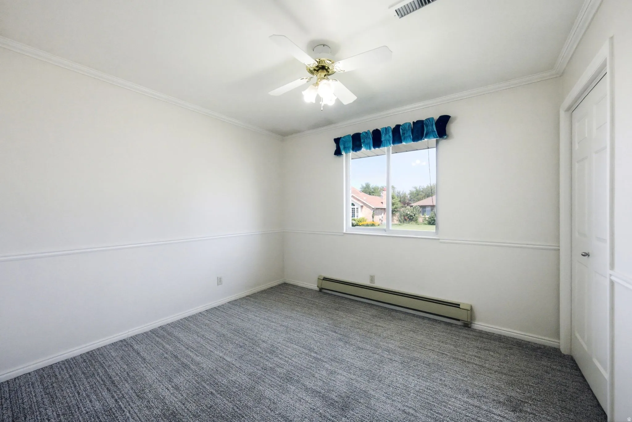 White walls with chair rail molding, ceiling fan with integrated lighting, gray patterned carpet, and a white paneled door