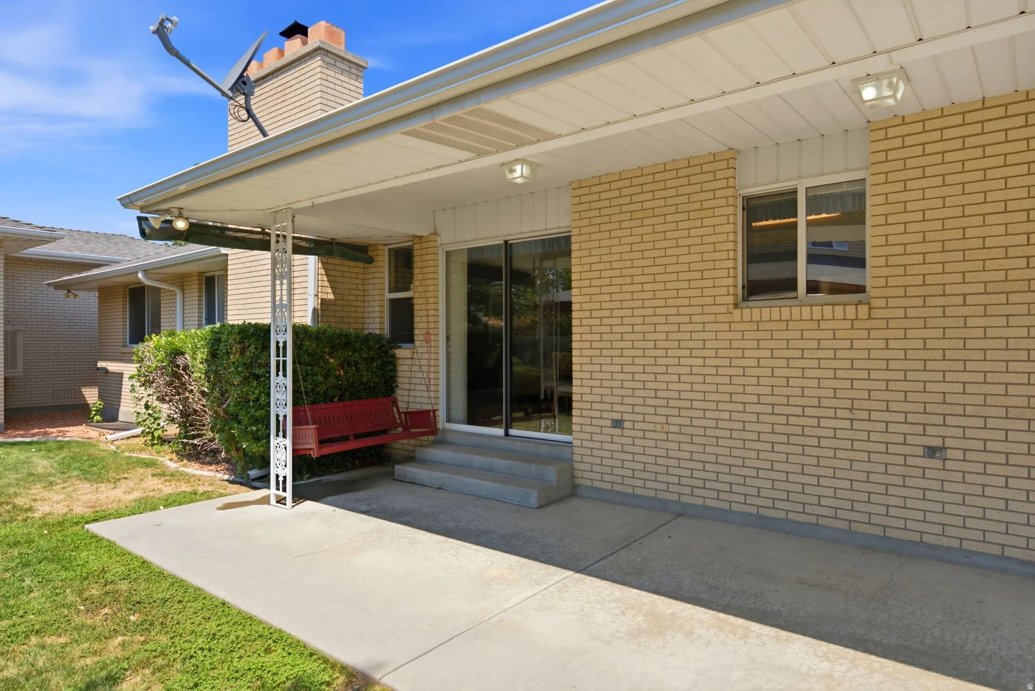 Covered patio with concrete flooring, brick exterior, sliding glass door, and a single window