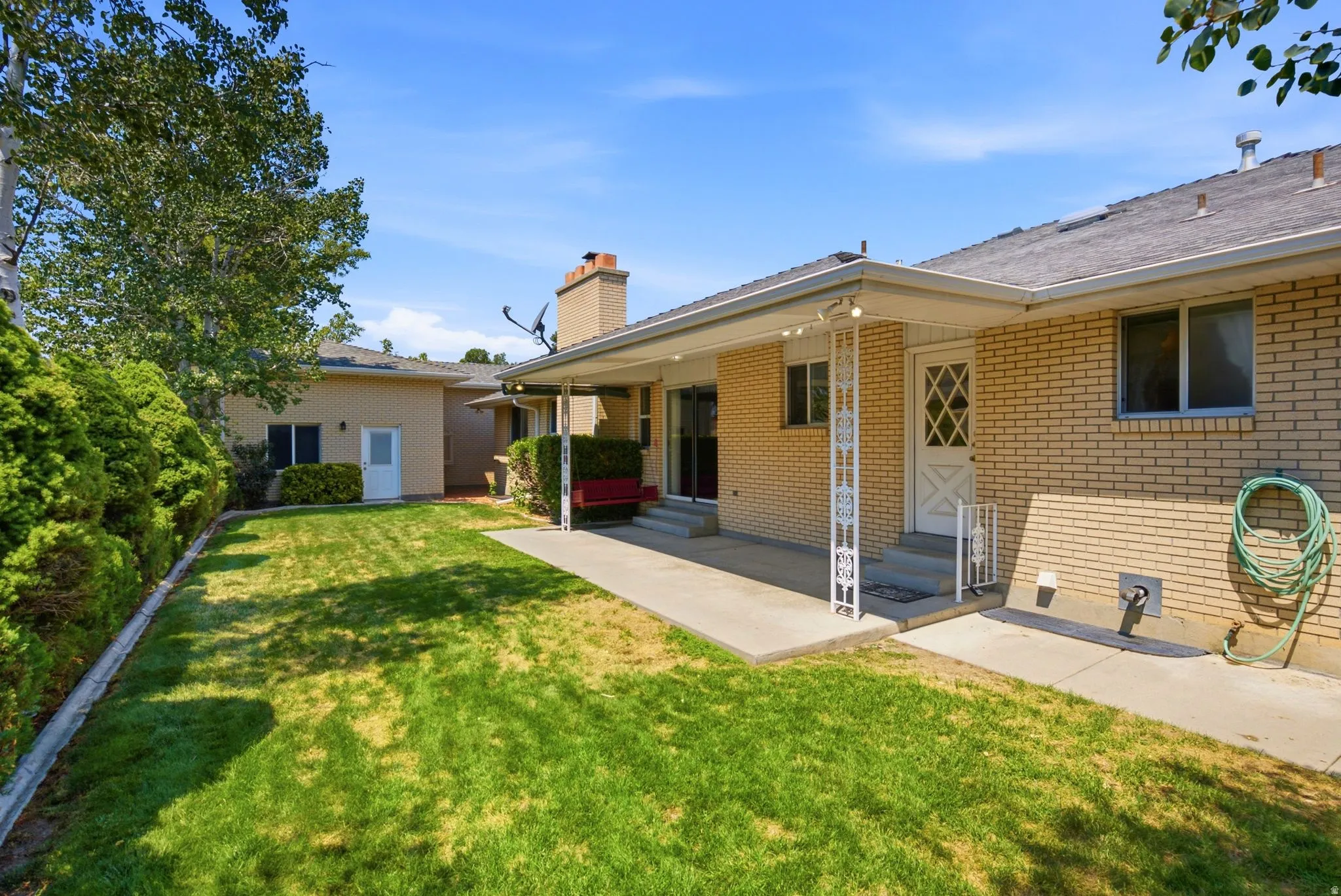 Expansive lawn area with mature perimeter landscaping, brick exterior, and covered patio space