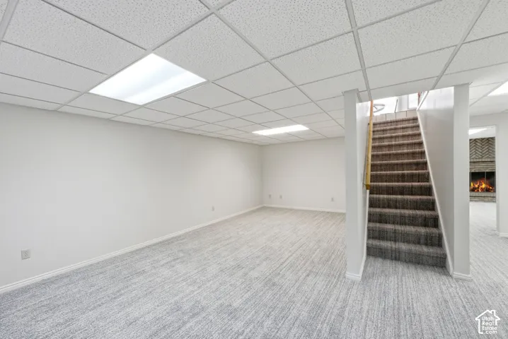 Spacious room with light-toned carpet, drop ceiling with integrated lighting, and a staircase with handrail