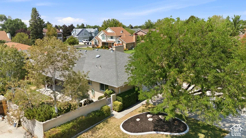 Pitched roof with gray shingles, mature perimeter trees, and a landscaped front yard with decorative rocks