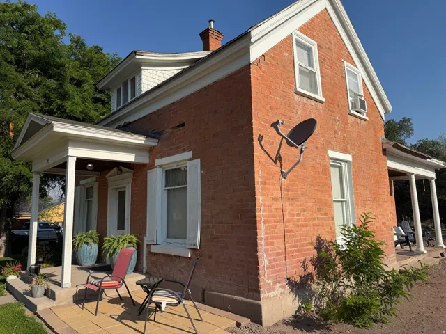 Exterior brick facade featuring white trim, a covered porch with white columns, and a dormer with white shake siding