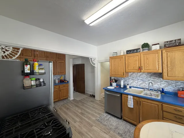 Kitchen featuring wood cabinetry, a mosaic tile backsplash, wood-finish flooring, and a stainless steel dishwasher