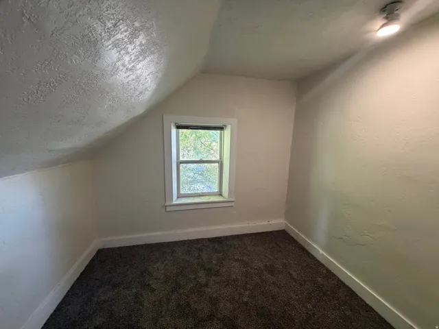 Windowed room featuring textured walls, sloped ceiling, track lighting, and dark carpeting