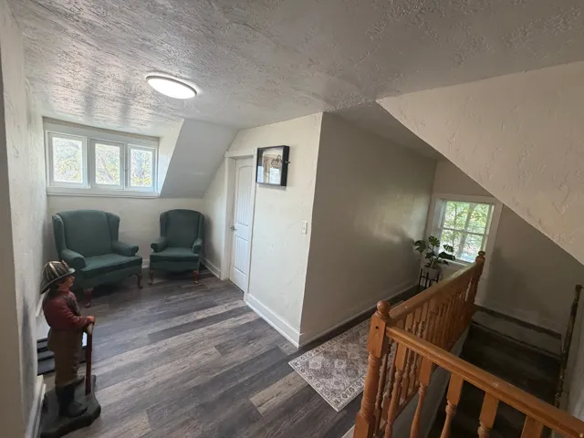 Attic landing featuring wood-finish flooring, a white trim window, a wood handrail, and a flush-mount ceiling light