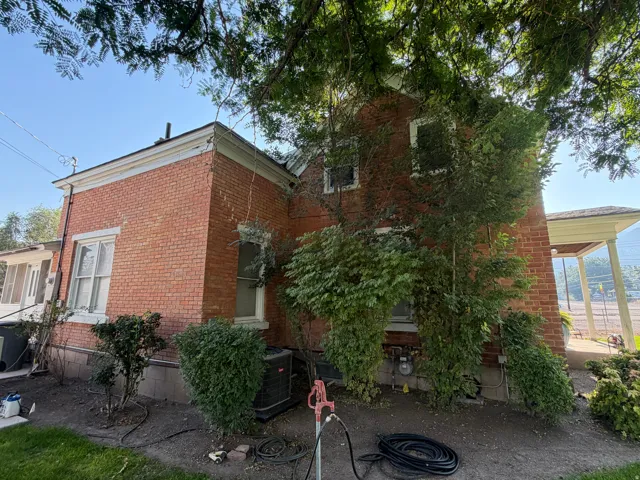 Brick exterior with white trim, featuring multiple windows, established foundation plantings, and mature overhead trees