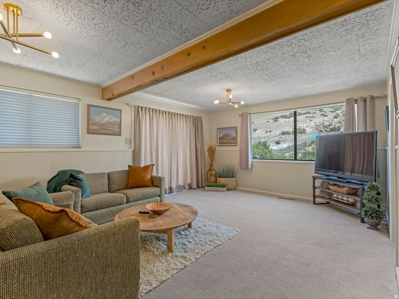 Expansive living area featuring carpeted flooring, a large picture window, and a wood beam ceiling accent