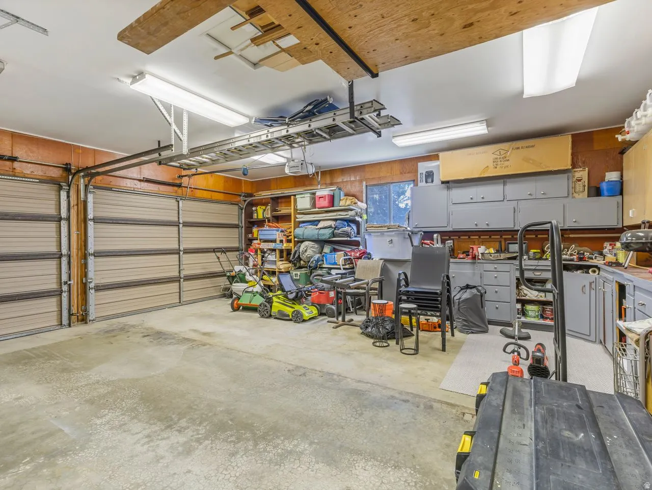 Spacious garage featuring two overhead doors, overhead storage racks, recessed lighting, built-in cabinetry, and a work surface