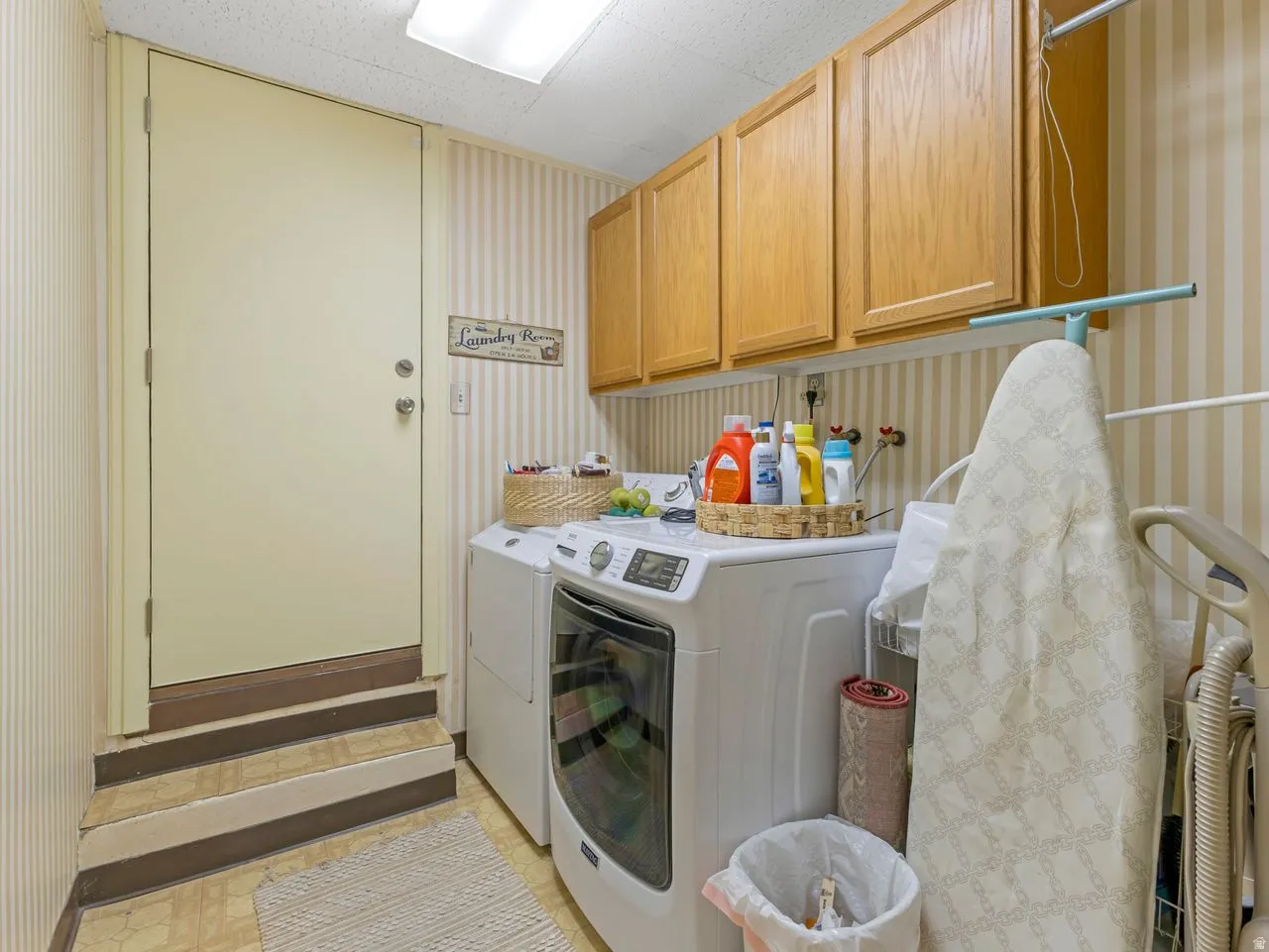 Laundry area featuring wood-finish cabinetry, a white built-in laundry tub, and striped wall covering