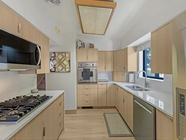 Light wood-finish cabinetry with modern hardware, stainless steel appliances, light-toned countertops, wood-finish flooring, and a rectangular window
