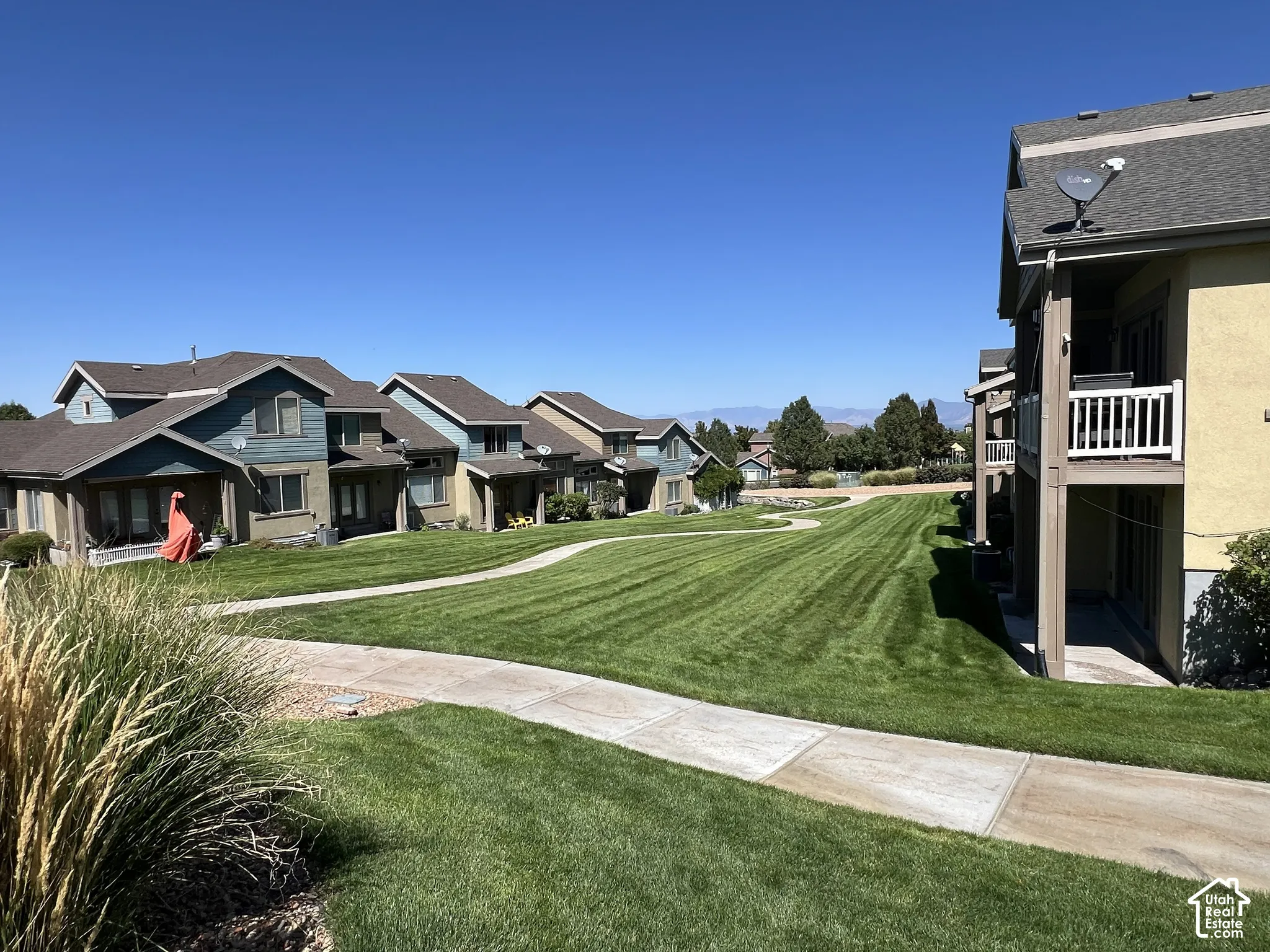 Manicured green space with a winding pathway, surrounded by multi-story residences featuring balconies and patios