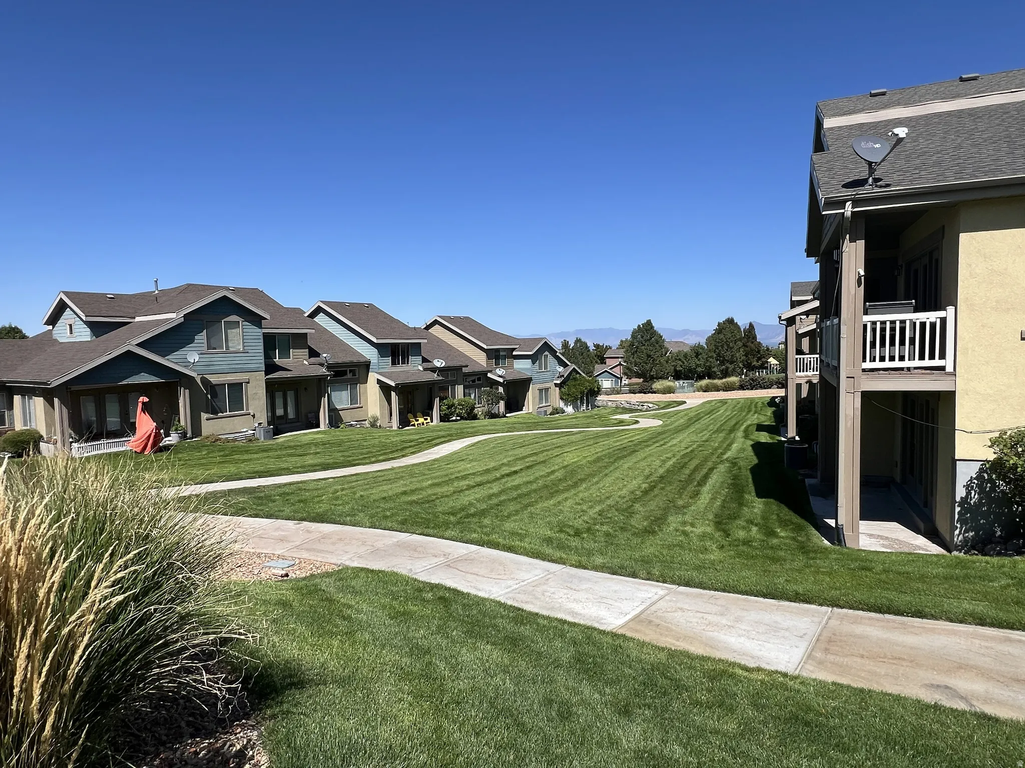 Manicured green space with a winding pathway, surrounded by multi-story residences featuring balconies and patios