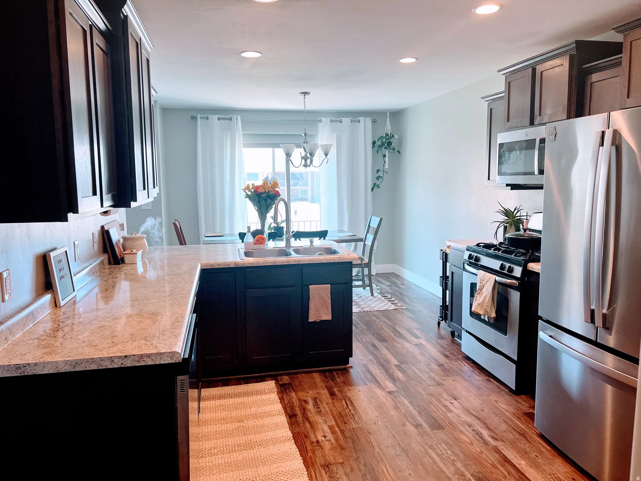 Kitchen featuring dark cabinetry, light-toned countertops, wood-finish flooring, recessed lighting, and stainless steel appliances