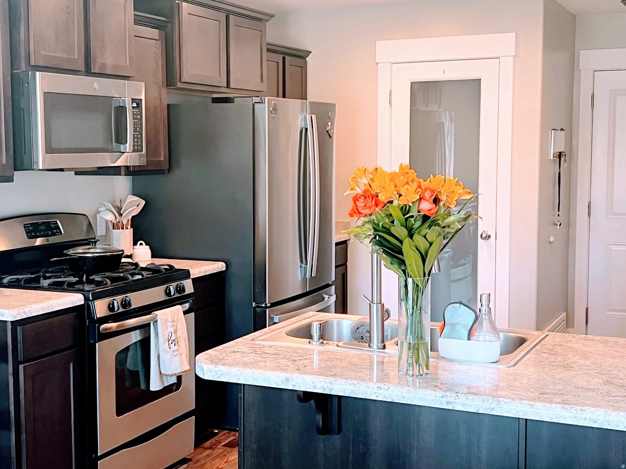 Stainless steel appliances, dark wood-finish cabinetry, light-toned countertops, and a double basin sink
