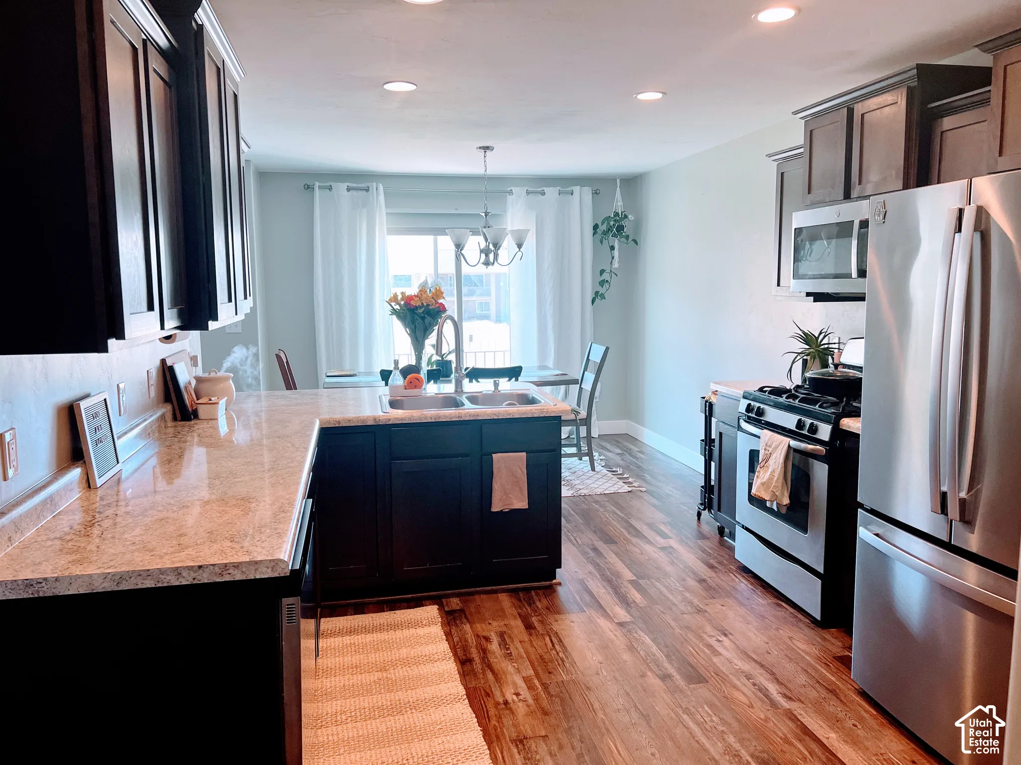 Kitchen featuring dark cabinetry, light-toned countertops, wood-finish flooring, recessed lighting, and stainless steel appliances