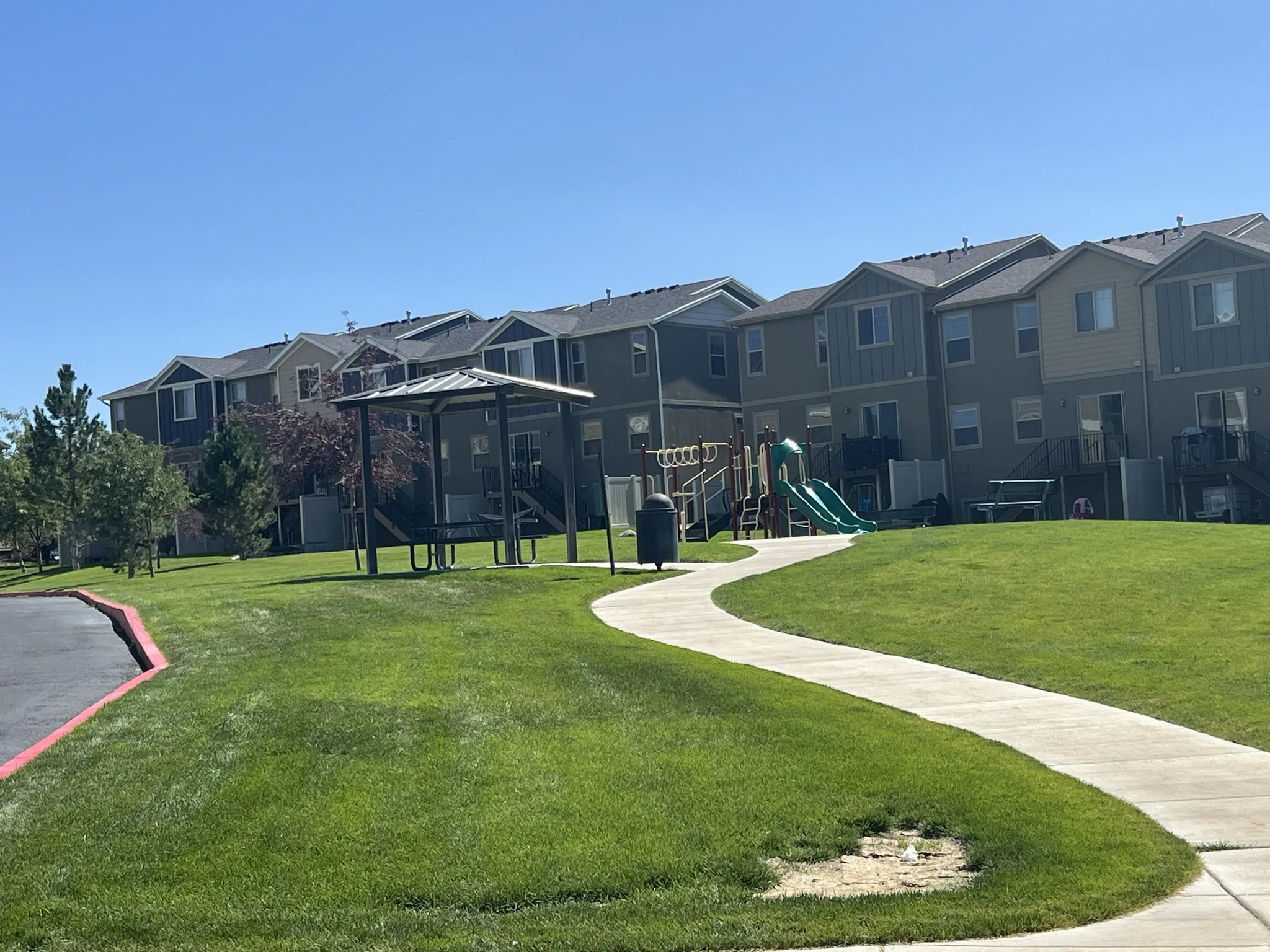Community green space featuring a paved walkway, covered picnic area, and a children's play structure