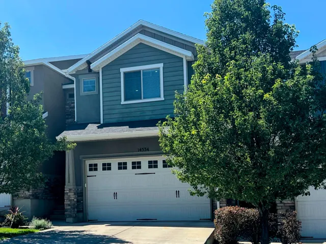 Townhome exterior featuring a two-car garage, stone accent siding, and mature trees