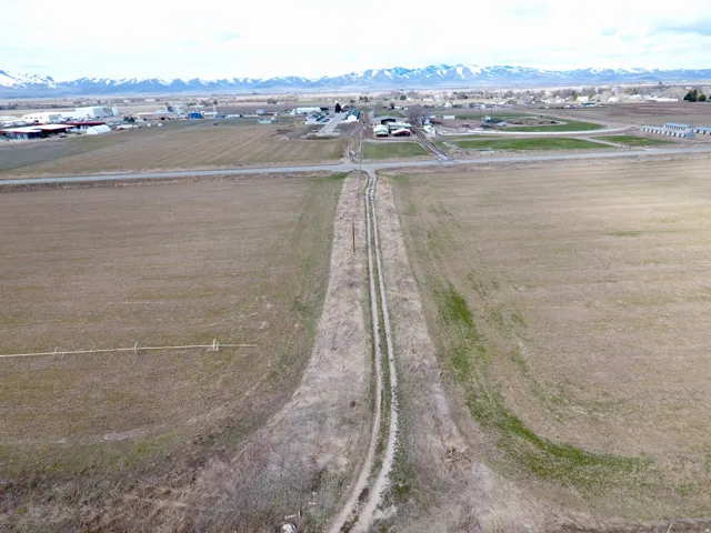 Expansive undeveloped land featuring a dirt road, irrigation equipment, and distant mountain ranges