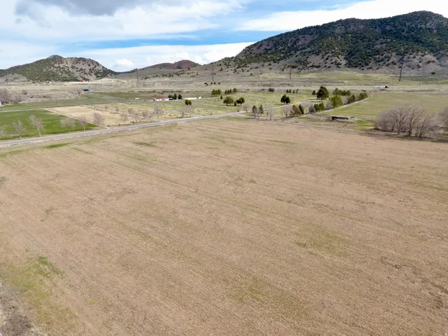 Expansive undeveloped land featuring a rural road, distant structures, and mountainous backdrops