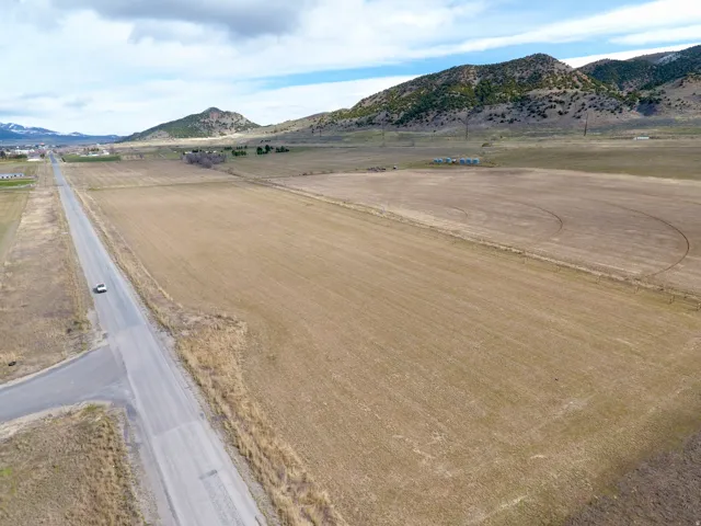 Expansive agricultural land featuring a gravel road, distant mountainous terrain, and rural structures
