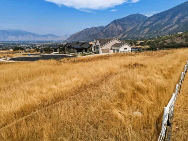Expansive acreage featuring golden native grasses and rustic fencing, with a residence, detached structures, and water feature nestled against dramatic mountain backdrop