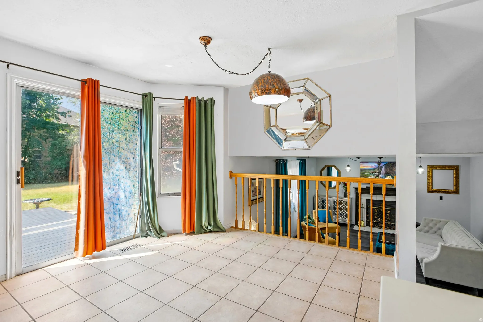 Tile flooring, sliding glass door, overhead pendant lighting, wood railing, and a decorative octagonal mirror