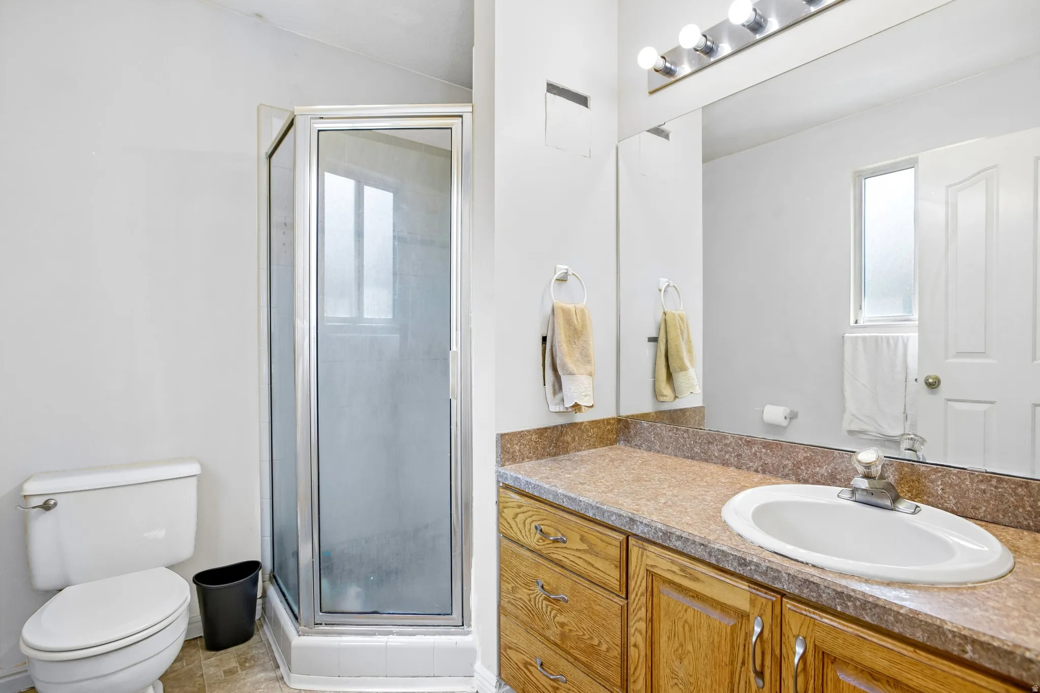 Bathroom featuring a corner shower enclosure, single vanity with wood-finish cabinetry, integrated sink, and an expansive mirror