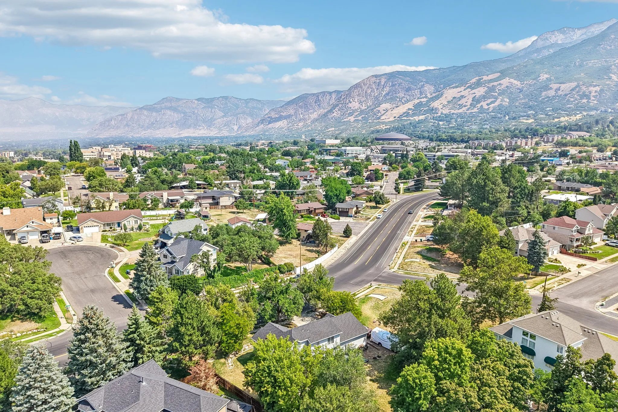 Residential area featuring mature trees, paved roads, and distant mountain backdrops